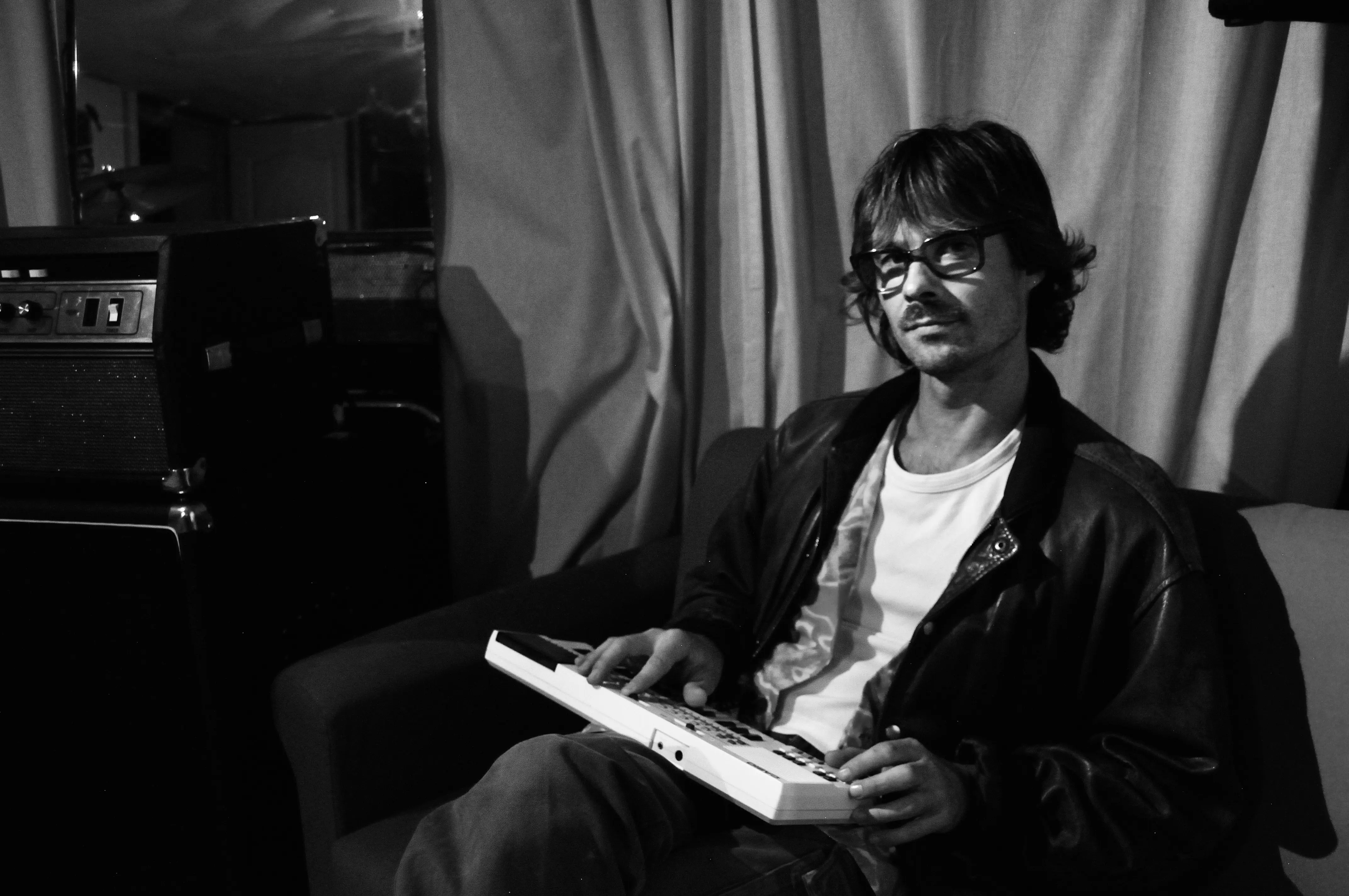Nicolas Soulatre composing music in his recording studio, seated with a MIDI keyboard in a black and white portrait.